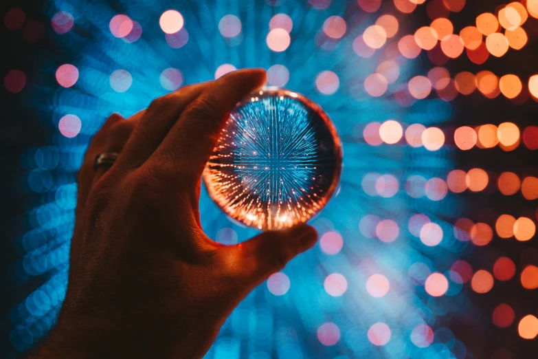 a person holding a glass sphere with colorful lights in the background