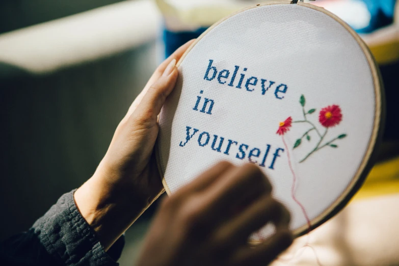 someone holding up an embroidered badge that says believe in yourself