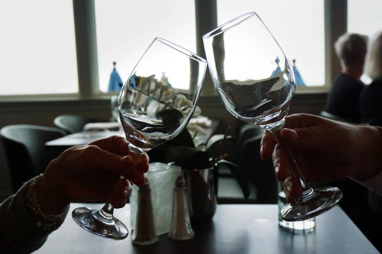 two people are holding wine glasses while seated at a restaurant