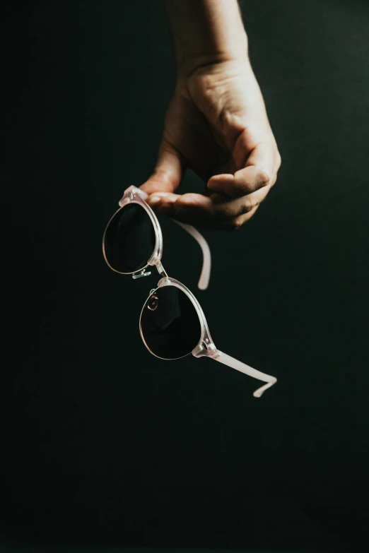 two sunglasses in hands that are over dark