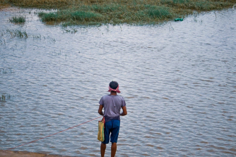 man walking a dog down a water way near a grassy area