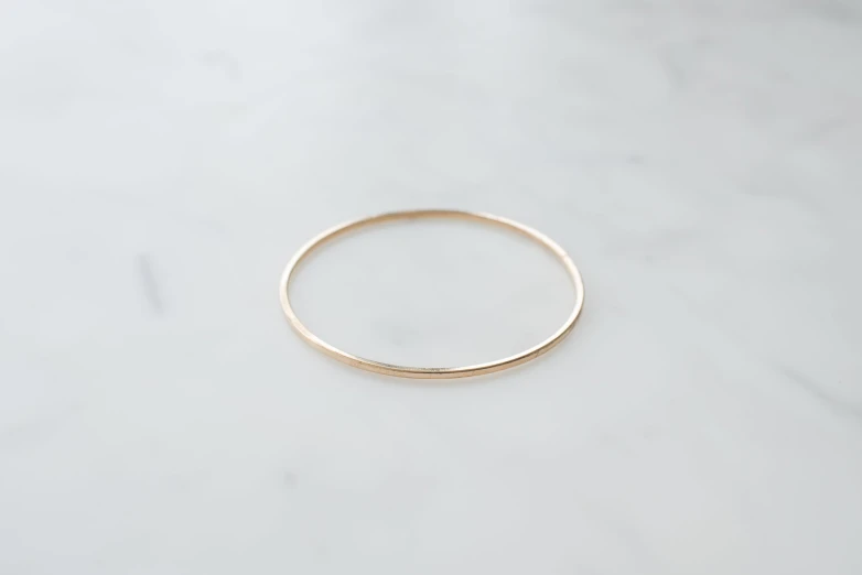 a plain gold wedding band is shown in front of a marble background