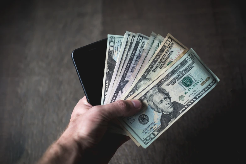 a man holding his phone to cash on a wooden surface