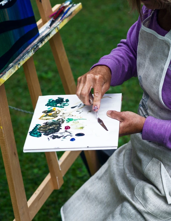 a woman is working on an easel on the grass