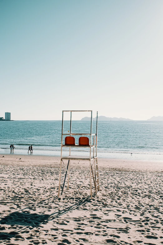 a lifeguard stand sits on the beach, with a person in the distance behind it