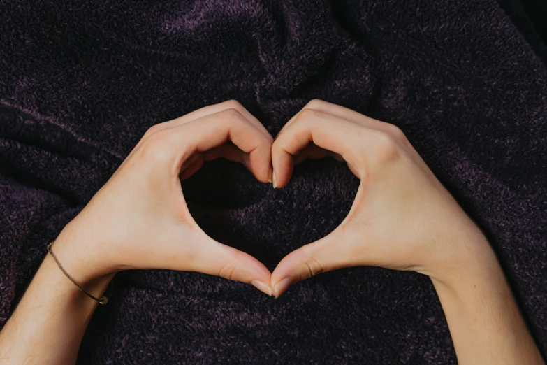 two hands creating a heart shape while laying on the bed