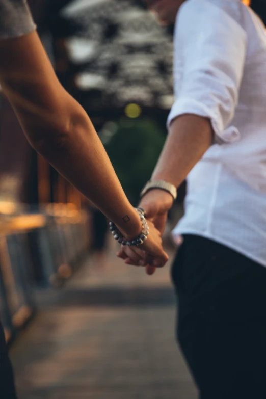 the two people hold hands while walking on the sidewalk