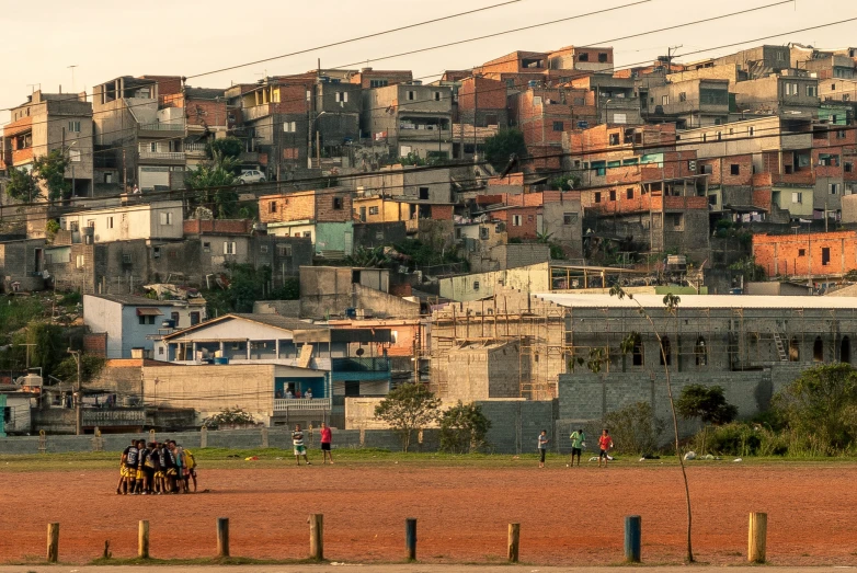 several people walking around on a dirt ground in front of a town