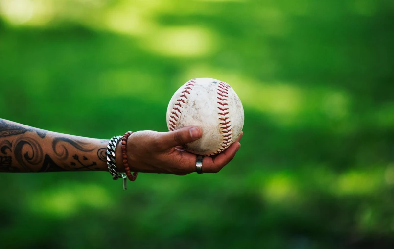 a hand that is holding a baseball in the grass