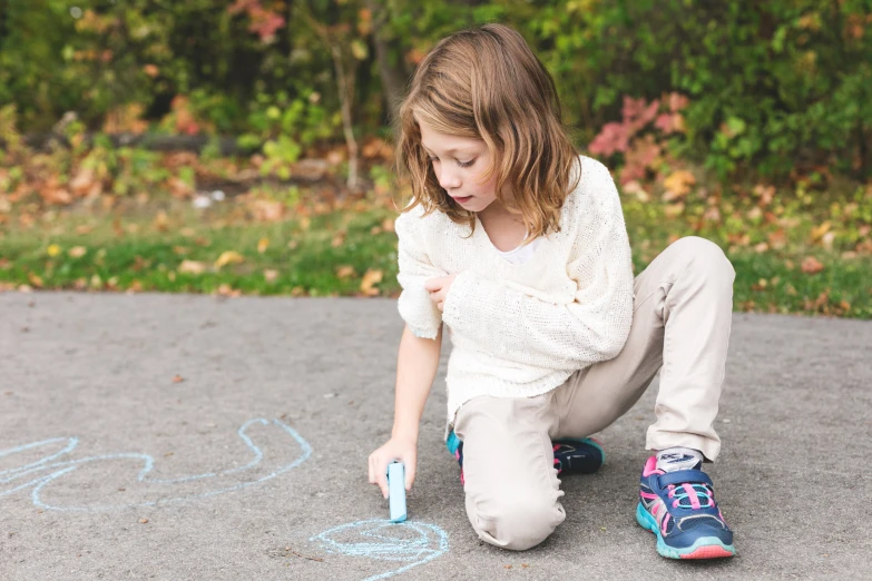 a girl sitting down on the ground draws with chalk