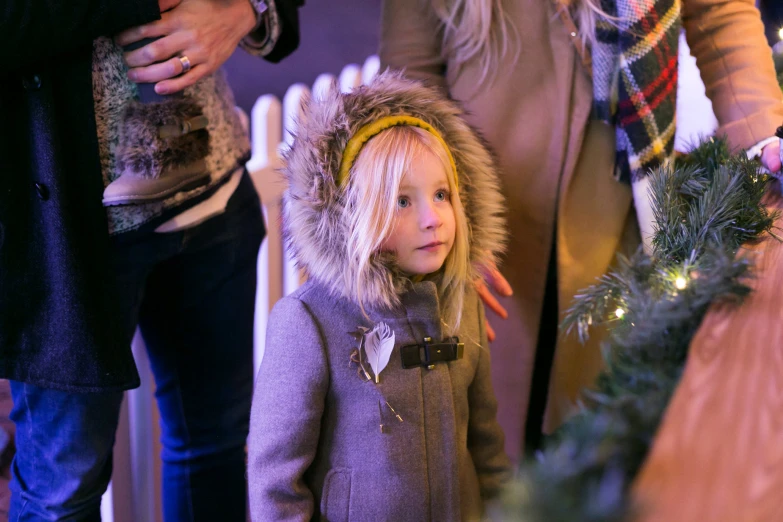 a little girl in winter clothing standing next to other adults