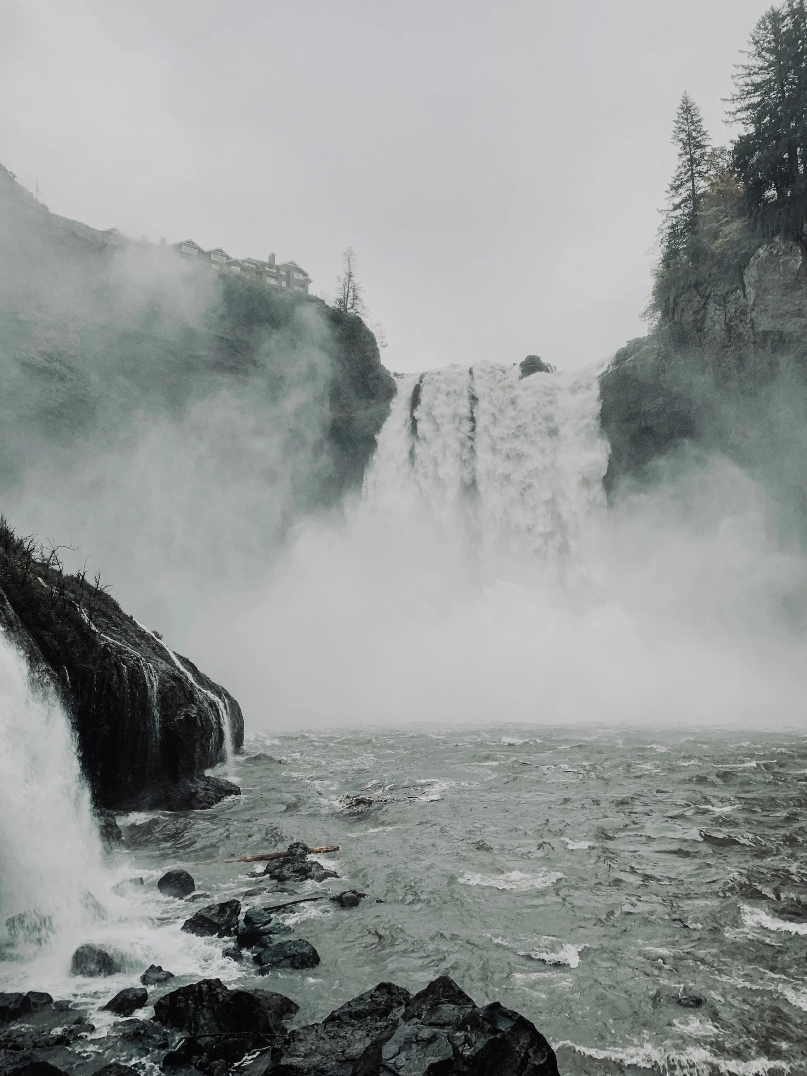 a large waterfall is on a misty day with mist rising