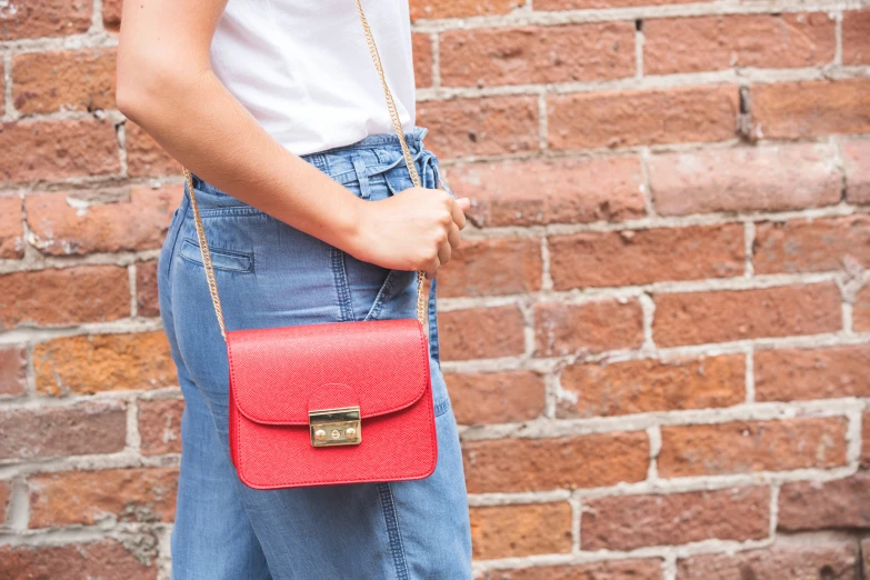 a young woman carrying a red purse next to a brick wall