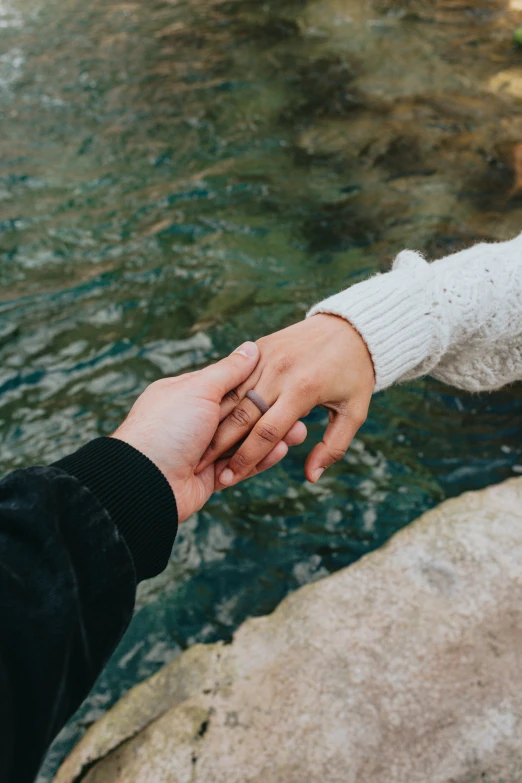 a person holding the hand of another persons'finger by a river