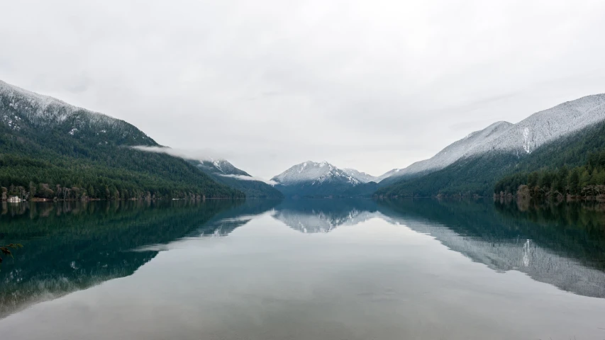 some mountains and snow covered trees by a lake