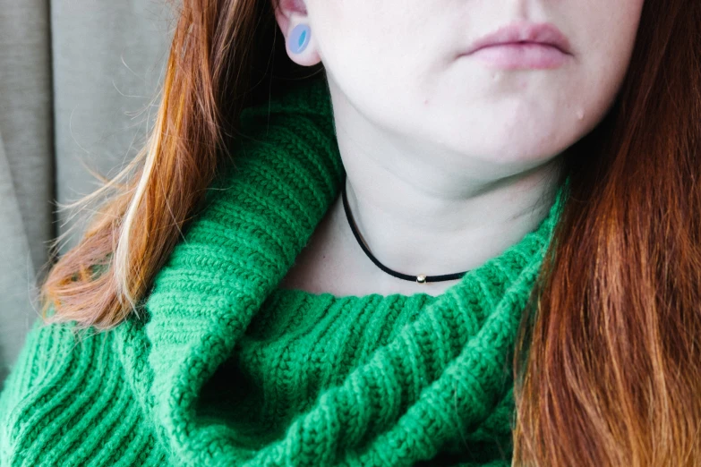 a woman wearing a green knitted sweater and wearing a black necklace