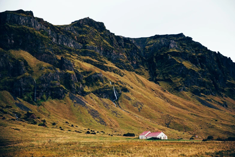 a house stands in a grassy valley near a huge mountain