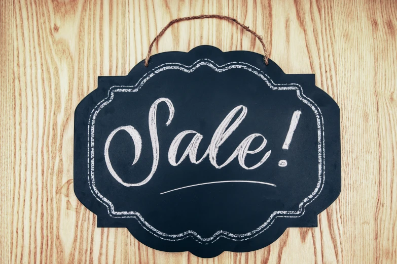 a black and white sale sign hanging on the side of a wooden wall