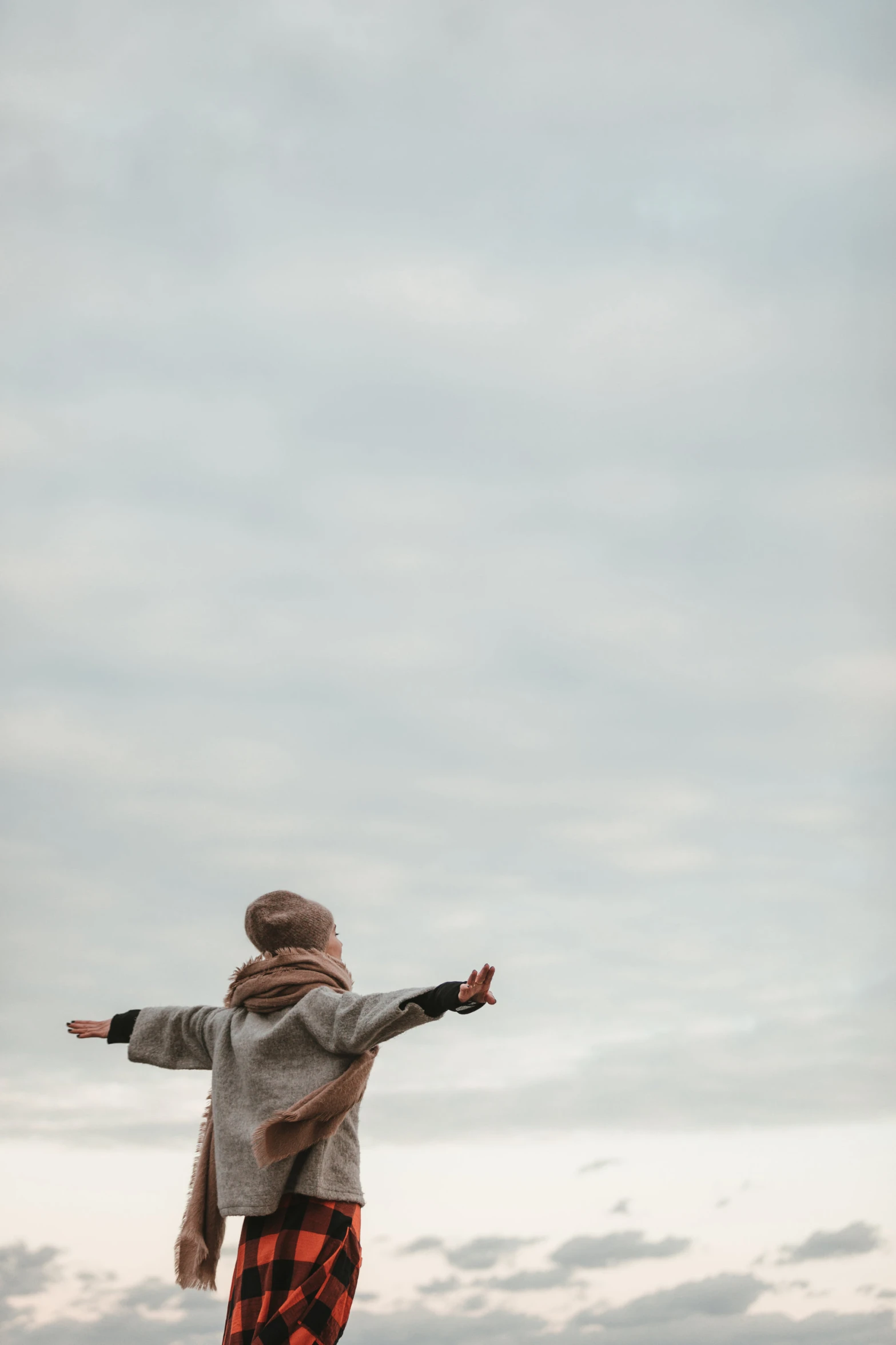 a young woman in gray jacket flying a kite