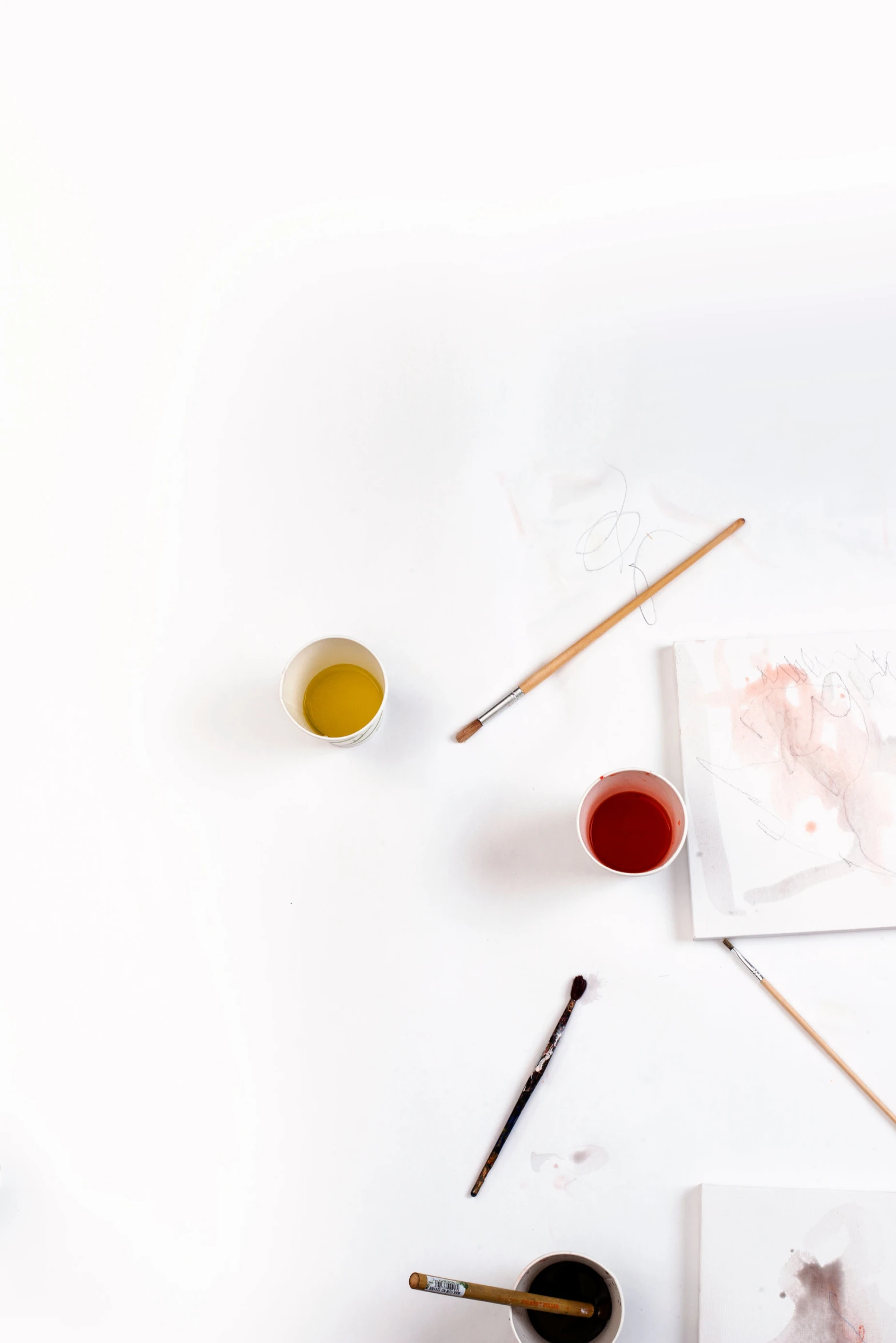 a table with various brushes, watercolor paints and a cup on it