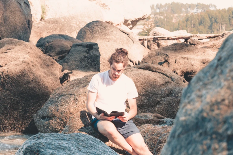 a man is sitting on some rocks by the water