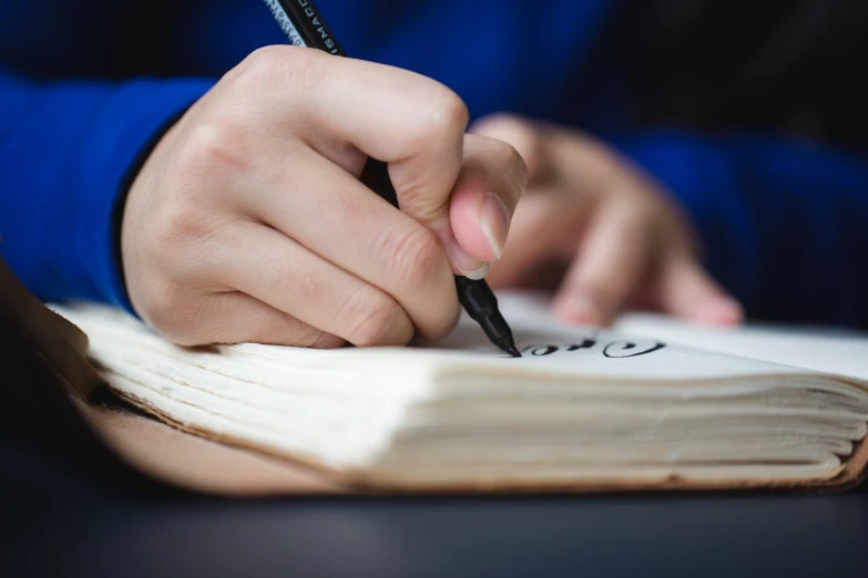 person writing with pen on book on table