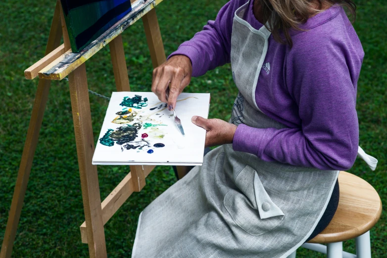 a woman in an apron with her hands on a paintbrush and canvas