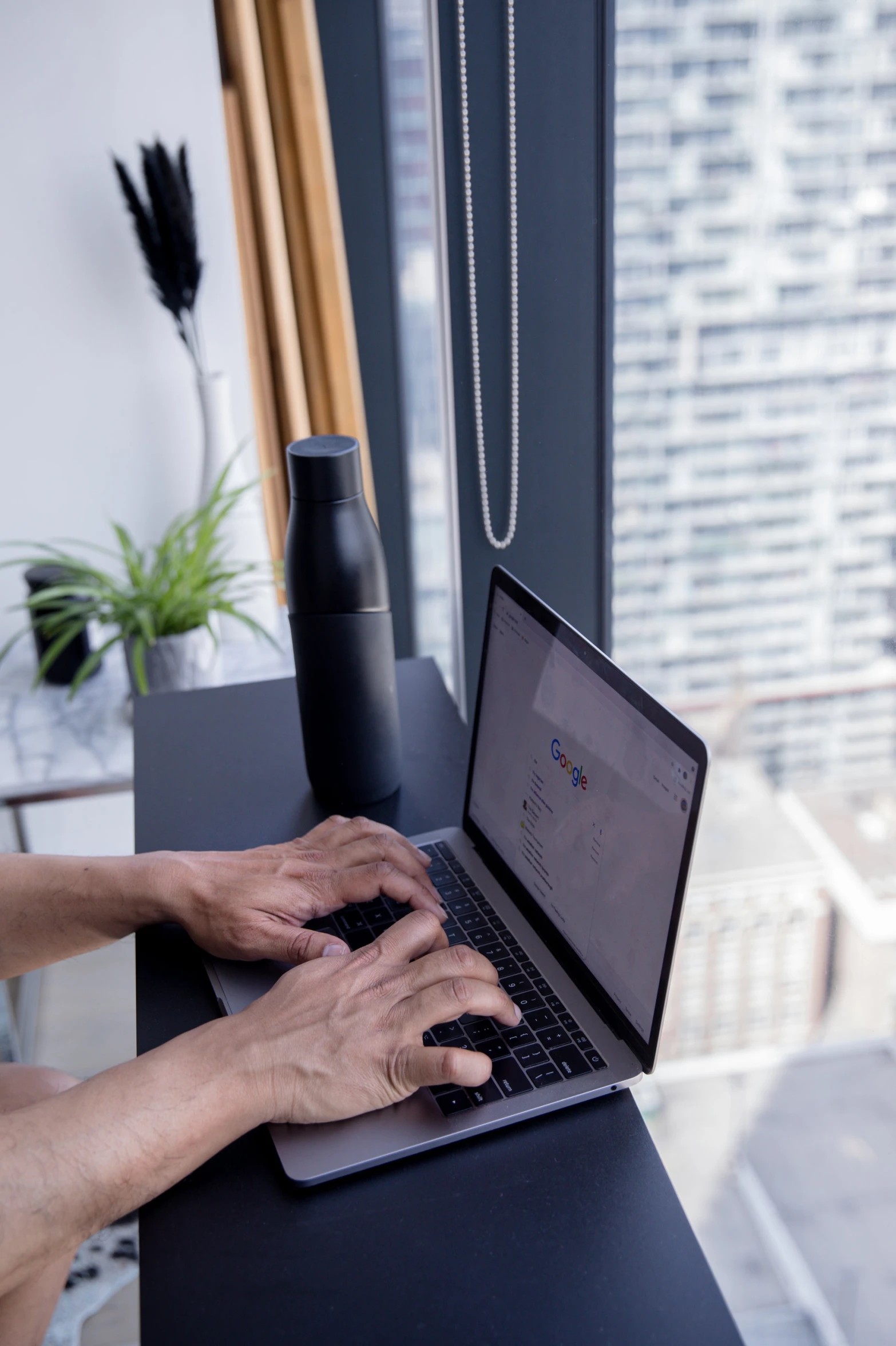 person typing on their laptop on a table next to a window