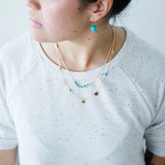 woman wearing two necklaces with blue, gold and green beads