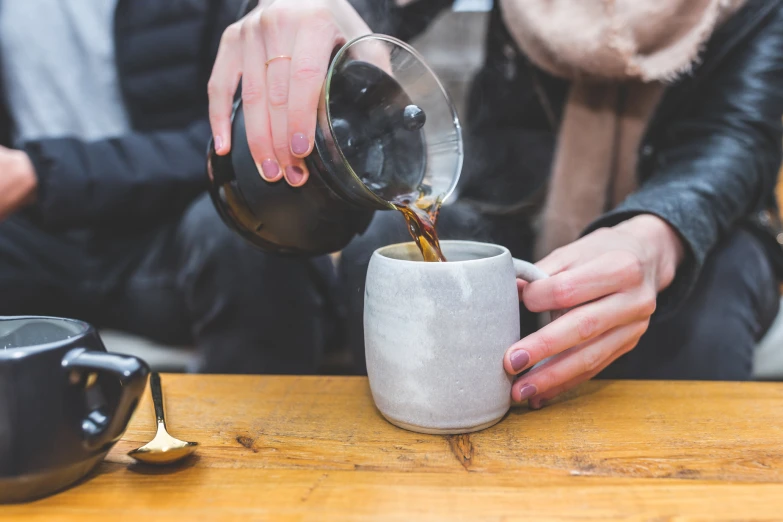 a person pouring coffee into a cup while another persons watch