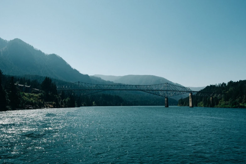 a view from a river with mountains and a bridge