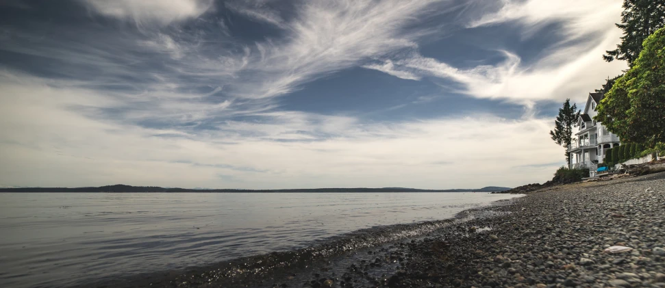 the view from a beach towards water with a house on the shore