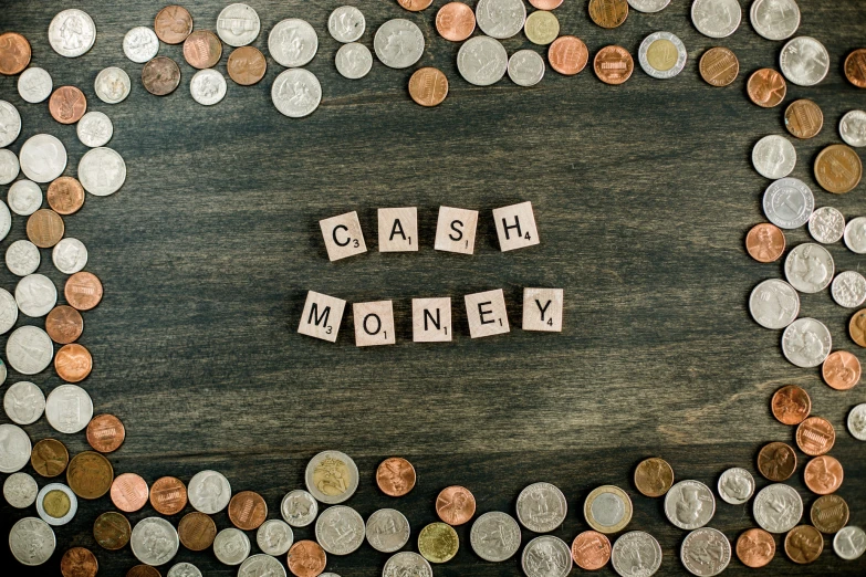 a pile of coins sitting next to wooden letter blocks that spell cash money