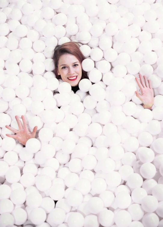 a smiling woman in a ball pit surrounded by white balls