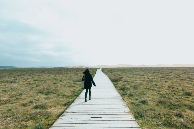 woman walking across a wooden walkway in a dry field