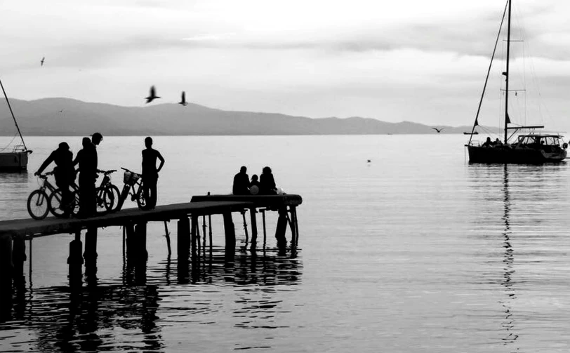 people on bicycles wait on a dock near a boat