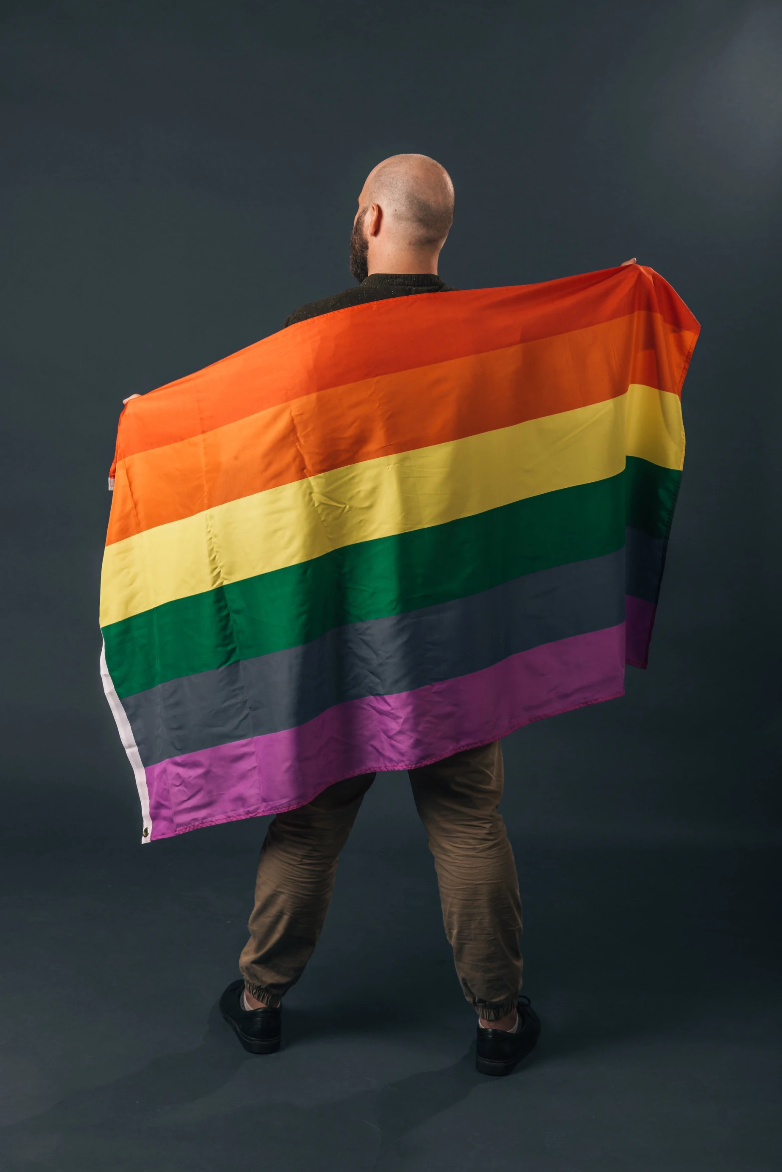 man holding large rainbow striped flag against grey background