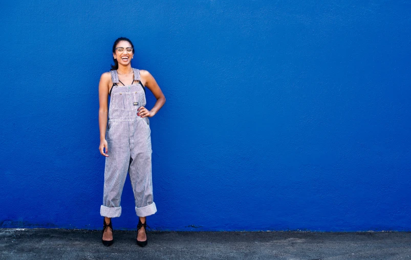 a woman in overalls poses next to a blue wall