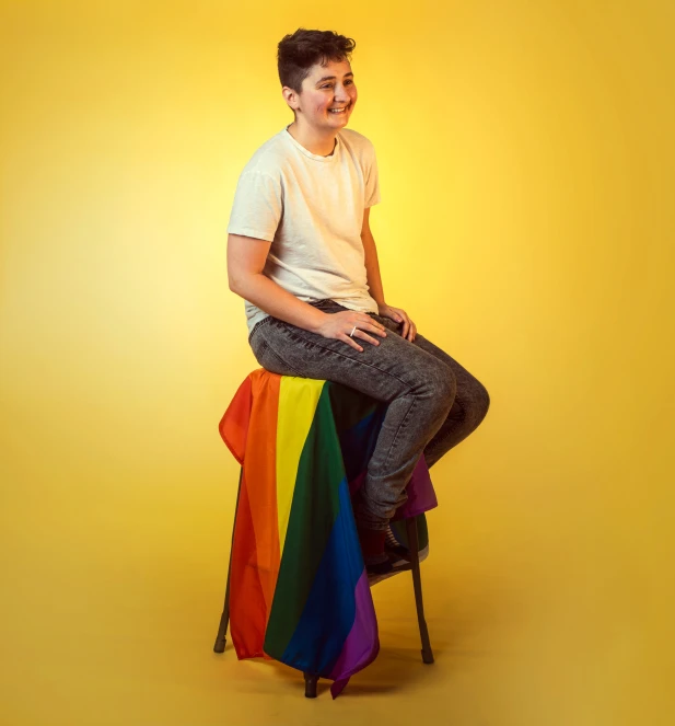 man in white shirt and black pants sitting on a rainbow colored chair