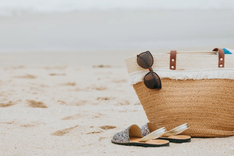 a beach bag on the sand with sandals and a blue towel