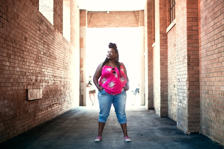 a woman wearing a pink top standing in an alley way