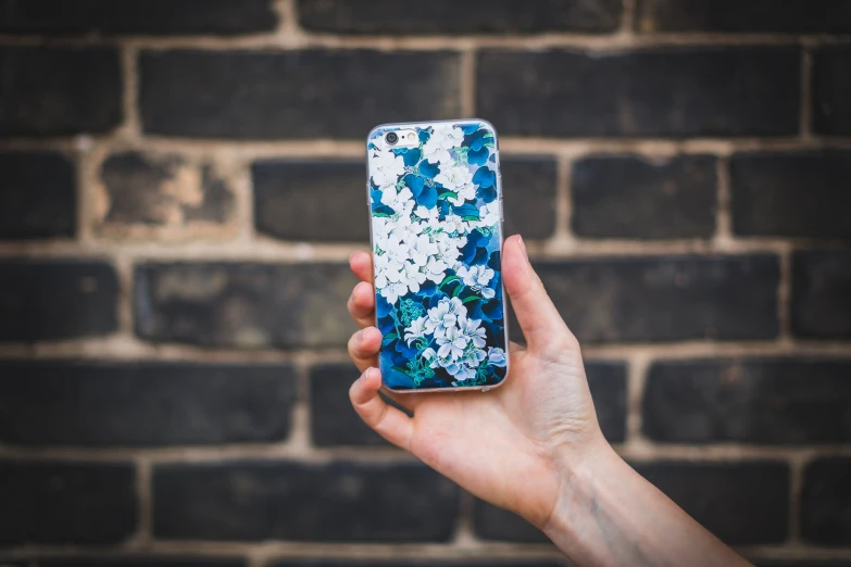 a hand holding a blue and white phone with white flowers