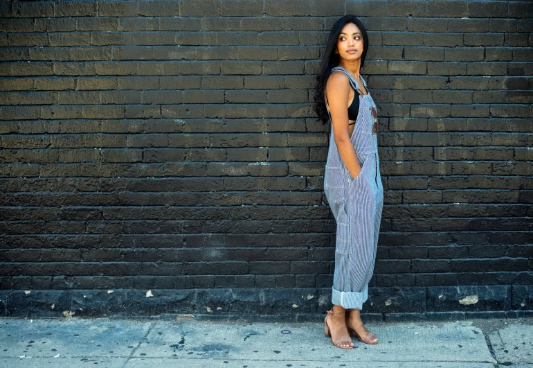 a young woman standing on the street in front of a brick wall