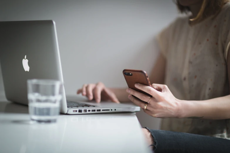 a woman sitting at a desk using a laptop and a cell phone