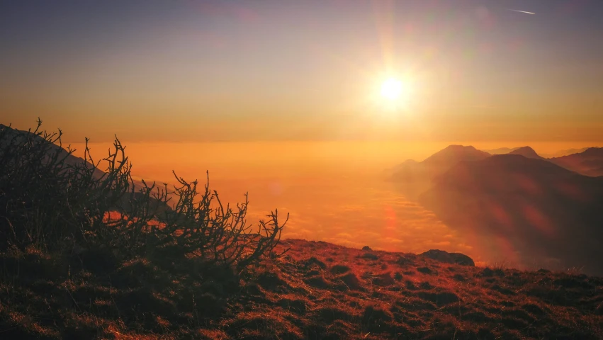 a sunset on the top of a grassy mountain