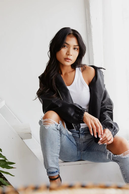 woman with ripped jeans leaning up on a chair in a white room