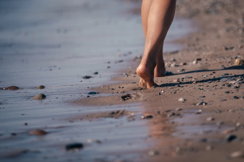 a persons feet walking in shallow water on a beach