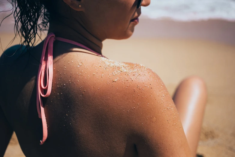 a girl with the pink straps on is sitting down on a beach