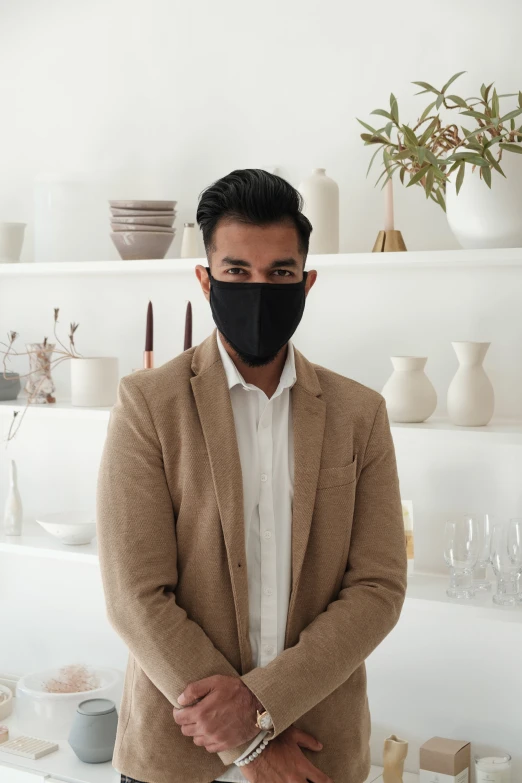 a man in a black face mask standing near some white vases