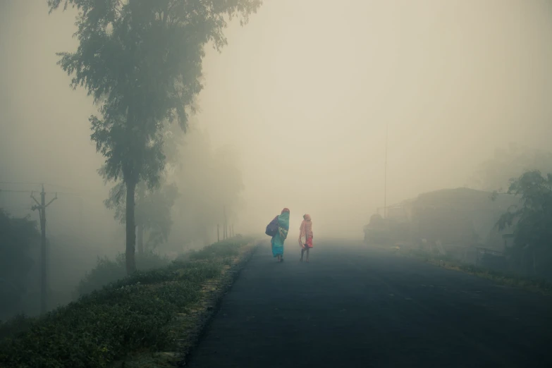 three people walking down a foggy road in front of some houses